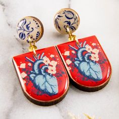 two red and blue earrings with flowers on them sitting on a marble counter top next to gold ear wires