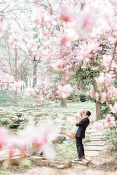 a man and woman are kissing in front of some pink flowers on the tree's branches