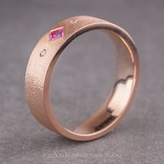 a rose gold wedding ring with a pink sapphire stone and diamond set in the center