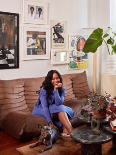 a woman sitting on top of a brown couch next to a dog and potted plant