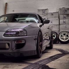 a grey sports car parked in a garage next to pallets of boxes and other items