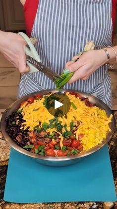 a woman in an apron is cutting vegetables into a large skillet on a blue mat