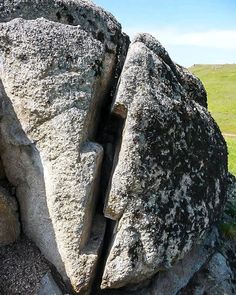 a large rock with some rocks sticking out of it's sides and grass in the background