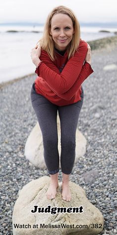 a woman sitting on top of a rock next to the ocean with her arms crossed