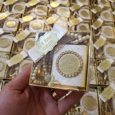 a hand holding a gold and white box with some pearls in it on a table