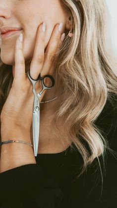 a woman holding a pair of scissors up to her face while wearing a black shirt