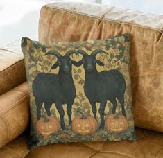 two black goats standing next to each other on a brown couch with pumpkins and leaves