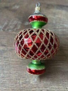 two red and green christmas ornaments hanging on a wooden table with one ornament in the shape of a ball