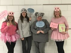 three women in pig costumes holding signs and standing next to each other against a white brick wall