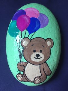 a painted rock with a teddy bear holding balloons