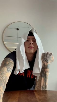 a man with tattoos and a towel on his head sitting at a table in front of a mirror