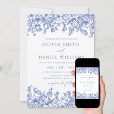 a person holding up a cell phone next to a wedding card with blue flowers on it