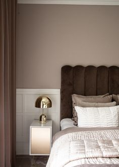 a bedroom with a brown headboard and white bedding, gold lamp on nightstand