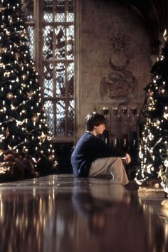 a woman sitting on the floor in front of christmas trees looking at her cell phone