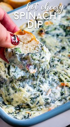 a hand holding a piece of bread over a casserole dish with spinach and cheese