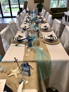 the table is set with white linens and place settings for an ocean themed celebration