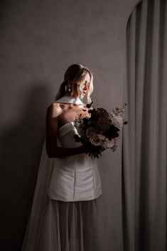 a woman standing in front of a curtain holding a bouquet