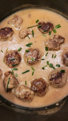 some meatballs and gravy in a pot with green onions on the side