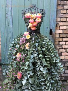 a dress made out of flowers sitting on top of a pile of greenery next to a blue door