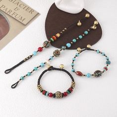 three different bracelets with beads and charms on top of a white table next to a pair of eyeglasses