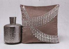 a silver vase sitting next to a brown pillow