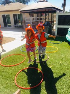 two children in life vests playing with hula hoop rings on the grass outside