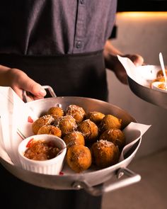 a person holding a pan full of food with dipping sauces on the side and other dishes in front of them