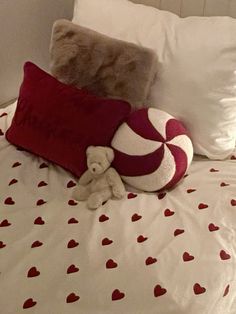 a teddy bear sitting on top of a bed next to pillows and a pillow with hearts