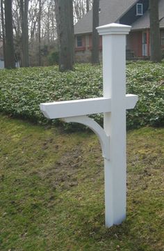 a white cross is in the grass near some bushes and trees with a house in the background