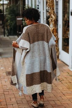 a woman walking down the street wearing a brown and white blanket