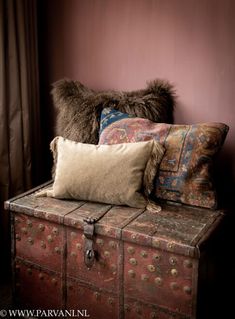 an old trunk with several pillows on it and a fur pillow sitting on top of it