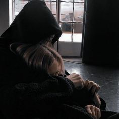 a woman sitting on the floor in front of a window wearing a black hoodie