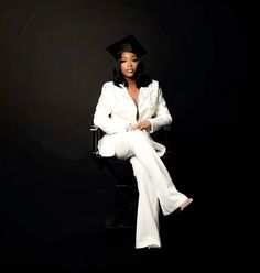 a woman sitting on top of a chair wearing a white suit and black graduation hat