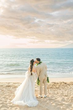 a bride and groom kissing on the beach in front of the ocean at their wedding