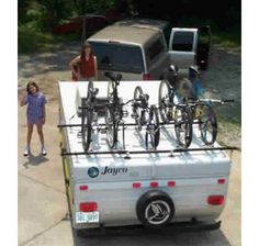 a white truck with bicycles on the back and two girls standing in front of it