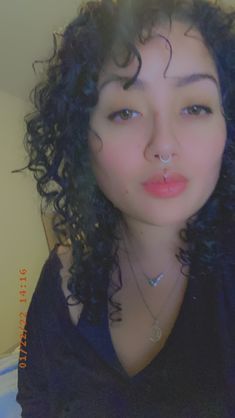 a woman with curly hair and piercings on her nose is posing for the camera