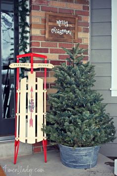 a small christmas tree sitting next to a wooden sled with a merry christmas sign on it