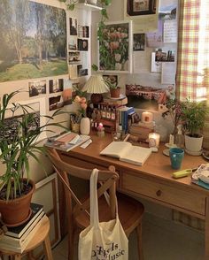 a wooden desk topped with lots of books next to potted plants and pictures on the wall