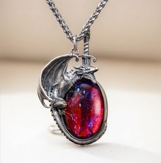 Embrace your inner strength and mythical allure with this stunning handcrafted dragon necklace. The dragon, made of 925 sterling silver, wraps protectively around a mesmerizing "Dragon's Breath" stone, which shimmers with an otherworldly mix of fiery reds and deep purples, reminiscent of mystical flames. The intricate detailing of the silver dragon captures its fierce yet elegant nature, and the sword behind the dragon adds an element of bravery and protection. The necklace hangs from a durable titanium chain, ensuring lasting quality and comfort.  This unique piece is perfect for fantasy lovers, dragon lover, or anyone looking to add a touch of magic to their jewelry collection. Material: Pendant: Sterling silver(dragon), dragon breath glass Chain: 22 inches titanium Dragon Breath, Silver Dragon Necklace, Jewelry Purple, Dragons Breath, Dragon Bracelet, Dragon Lover, Dragon Necklace, Magical Jewelry, Crystal Opal