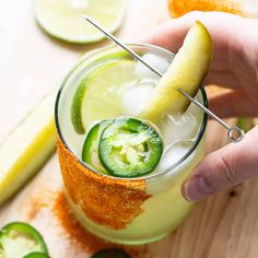 a person holding a pickle over a glass filled with cucumber and limeade