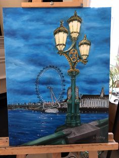 an easel with a painting of a street light and ferris wheel in the background