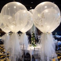 two clear balloons with white bows are sitting on top of tables in a banquet hall