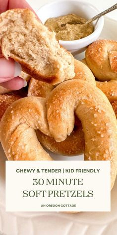 a person holding a piece of bread over some soft pretzels on a white plate