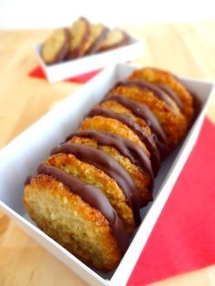 a box filled with chocolate covered donuts on top of a wooden table next to two red napkins