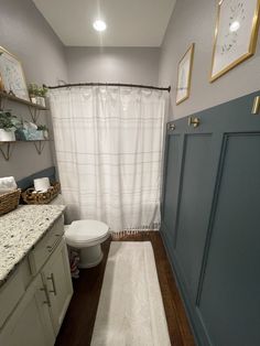 a bathroom with a toilet, sink and shower curtain in it's corner next to a white rug