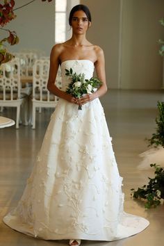 a woman in a white wedding dress holding a bouquet and standing on the floor with chairs behind her