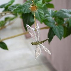 a glass dragon ornament hanging from a tree branch with flowers in the background