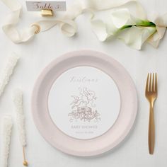 a table setting with white flowers and gold cutlery, place cards and napkins