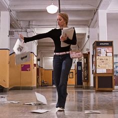 a woman in black shirt and jeans throwing papers into the air with her arms outstretched