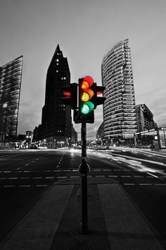 a traffic light sitting on the side of a road in front of tall buildings at night